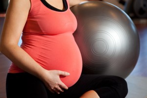A young pregnant woman doing relaxation exercise using a fitness ball and holding her tummy